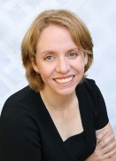 Head Shot of Georgie Lee. She is smiling, has blonde hair and is wearing a spiffy black dress